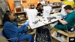 Myreshk Buckingham, left, fills bottles of hand sanitizer at Cleveland Whiskey, March 31, 2020, in Cleveland. Workers will be filling dozens of one gallon jugs and thousands of 4-ounce bottles of hand sanitizer made for the Cleveland Clinic.