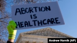 Žena u liječničkoj uniformi drži poster na kojem piše "Abortus je zdravstvena zaštita" dok zagovornici prava na abortus i demonstranti protiv abortusa demonstriraju ispred Vrhovnog suda SAD-a, srijeda, 1. decembra 2021., u Washingtonu. (AP Photo/Andrew Harnik)