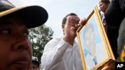 លោក សម រង្ស៊ី ប្រធាន​គណបក្ស​សង្គ្រោះ​ជាតិ (កណ្តាល) និយាយ​ទៅ​កាន់​កម្មករ​រោងចក្រ​កាត់ដេរ​នៅ​ក្បែរ​ទីលាន​ប្រជាធិបតេយ្យ ដោយសមាជិកា​គណបក្សរបស់​​លោកមួយ​រូប​​កាន់​រូបថត​កម្មករ​រោងចក្រ​ម្នាក់​ដែល​ត្រូវ​បាន​បាញ់​ស្លាប់​កាលពី​ដើម​ឆ្នាំ​នេះ ក្នុង​ទីក្រុង​ភ្នំពេញ​នៃ​ប្រទេស​កម្ពុជា។ រូបថត​នេះ ថត​នៅ​ថ្ងៃទី១​ខែឧសភា ឆ្នាំ២០១៤។ (AP Photo)