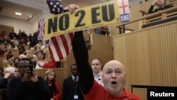 FILE - A demonstrator holds a pro-Brexit sign and a U.S. flag, as the speech by the Mayor of London, Sadiq Khan, is interrupted at the Fabian Society New Year Conference, in central London, Britain Jan. 13, 2018.