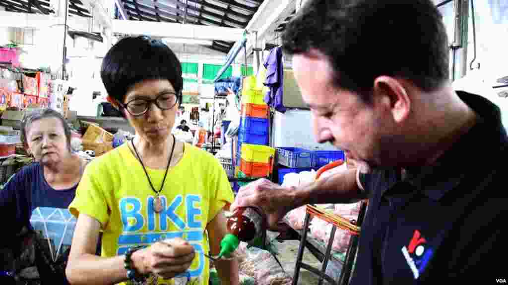 VOA Correspondent Steve Herman pours Sriracha hot sauce onto a spoon for Aree Khajonrungruang to try in the Si Racha central food market. (Z. Aung/VOA)