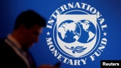 FILE - A participant stands near a logo of IMF at the International Monetary Fund - World Bank Annual Meeting 2018 in Nusa Dua, Bali, Indonesia, Oct. 12, 2018. 