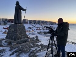 Reporter VOA Henry Ridgwell mengambil gambar di samping patung Hans Egede, misionaris Kristen yang membawa Denmark ke Greenland, 14 Januari 2025. (Foto: Mikkel Noa Klein)