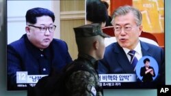 A South Korean marine passes by a TV screen showing file footage of South Korean President Moon Jae-in and North Korean leader Kim Jong Un, during a news program at the Seoul Railway Station in Seoul, South Korea, April 18, 2018.