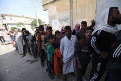 People stand in a queue to receive bread in the border town of Tal Abyad, Syria, Oct. 18, 2019.