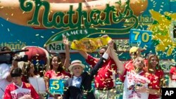 Joey Chestnut, right, is declared Nathan's Famous Fourth of July International Hot Dog Eating Contest men's competition winner, Monday, July 4, 2016, in New York.
