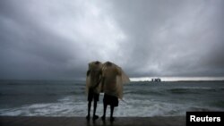 Two men use a plastic sheet to protect themselves from heavy monsoon rain as they stand by the sea in Colombo, Sri Lanka