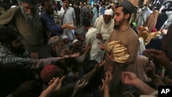 A worker distributes free traditional roti or bread among needy people at a restaurant, in Peshawar, Pakistan on April 16, 2023. (AP Photo/Muhammad Sajjad)