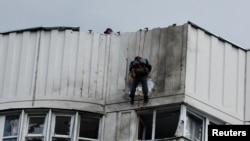 Seorang pekerja tampak membetulkan bagian yang rusak dari gedung apartemen di Moskow, Rusia, pada 30 Mei 2022. Gedung apartemen tersebut dikabarkan diserang oleh pesawat nirawak. (Foto: Reuters/Maxim Shemetov)