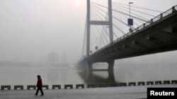 A resident walks along a street on the banks of the Songhua River near a highway bridge on a hazy day in Jilin province, Feb. 25, 2014.