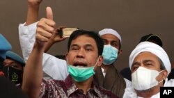 FILE - General secretary of the now-defunct Islam Defenders Front Munarman, left, who is also the lawyer of firebrand cleric Rizieq Shihab, right, gestures at reporters after Rizieq's questioning at the Regional Police Headquarters in Jakarta, Indonesia o