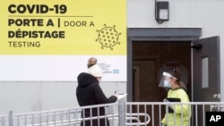 FILE - A health worker welcomes a woman to be tested for coronavirus at a clinic in Montreal, Canada, Dec. 6, 2020.