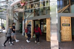 Shoppers walk into Pioneer Place shopping mall, which is still protected by wooden panels to prevent windows being smashed by ongoing protests in Portland, Ore., on June 5, 2021.