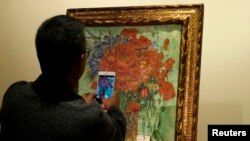Seorang pria mengabadikan lukisan Vincent van Gogh, "Vase with Daisies and Poppies", di balai lelang Sotheby di Hong Kong, 6 Desember 2014. (Foto: Reuters/Ilustrasi)