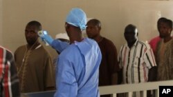 A health worker, center, takes the temperature of people to see if they might be infected by the Ebola virus inside the Ignace Deen government hospital in Conakry, Guinea, March 18, 2016.