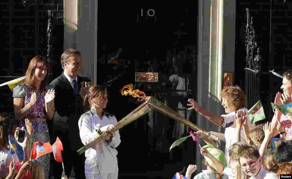 Britain&#39;s Prime Minister David Cameron (2nd L) and his wife Samantha (L) look on as Olympic torch bearer Florence Rowe (R) receives the flame from Kate Nesbitt (3rd L) in Downing Street, July 26, 2012. 