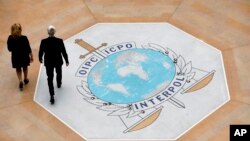 In this photo taken on Thursday, Nov.8, 2018 people walk on the Interpol logo at the international police agency headquarters in Lyon, central France.
