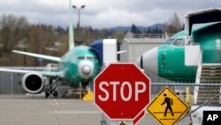 Des Boeing 737 MAX 8 sont garés derrière un panneau d'arrêt indiquant un passage à niveau dans une usine de production de Boeing Co., le lundi 8 avril 2019, à Renton, Etat de Washington, Etats-Unis. (AP Photo/Elaine Thompson)