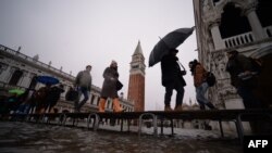 Visitors walk in flooded St-Mark square in Venice, in the morning of Nov. 17, 2019 prior an "acqua alta", or high water, of 160 centimeters (over five feet) expected at midday.
