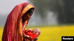 FILE - Monowara holds her 22-day-old grandson Arafat, as she walks through a mustard field on the outskirts of Dhaka.