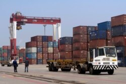 FILE - In this July 24, 2019, photo, workers watch as a truck passes by stacks of shipping containers at a port in Yingkou in northeastern China's Liaoning province.