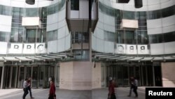 FILE - People are reflected in glass by the main entrance of BBC headquarters, in London, Britain, July 16, 2015.