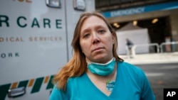 Registered Nurse Elizabeth Schafer, 36, of South St. Paul, Minn., stands for a portrait before entering Beth Israel Mount Sinai Hospital for her second day volunteering to combat the COVID-19 pandemic, Wednesday, April 1, 2020, in New York. (AP Photo/John Minchillo)