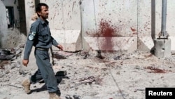 FILE - An Afghan policeman walks past a bloodstained wall after Taliban fighters stormed a government compound in Kandahar province, July 9, 2014. At least 16 police personnel were killed overnight in a Taliban attack in the province's Maiwand district.