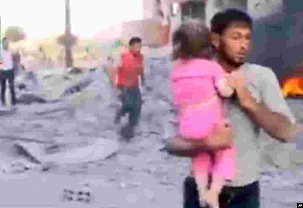This image taken from video obtained from the Shaam News Network shows a Syrian man carrying an injured child away from a missile strike in Raqqa, Syria, August 7, 2013.