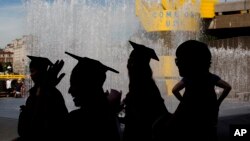 Students wearing their graduation gowns and caps are silhouetted as they stand beside a fountain on the southbank of the River Thames in London.