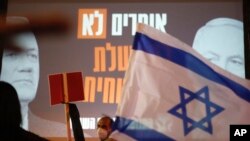A man holds a sign in front of a poster of Israeli Prime Minister Benjamin Netanyahu, right, and Benny Gantz that reads "Say no a corrupt government" during a protest at Rabin Square in Tel Aviv, Israel, May 2, 2020.
