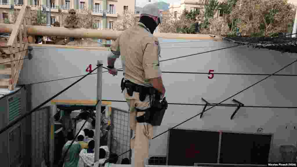 Un militaire norvégien veille sur les migrants qui débarquent du bateau &quot;Siem Pilot&quot; à Messine, Sicile, 6 ocotbre 2015 (Nicolas Pinault/VOA).
