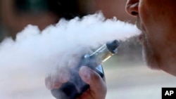 File - In this Aug. 28, 2019, file photo, a man exhales while smoking an e-cigarette in Portland, Maine. Oregon's public health physician said Wednesday, Sept. 4, 2019, that a person who contracted a severe respiratory illness and died after using…