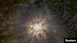 Orang-orang berdiri di sekitar kawah yang terbentuk akibat serangan rudal Rusia, di tengah serangan Rusia ke Ukraina, di desa Buda-Babynetska, di luar Bucha, dekat Kyiv, Ukraina 15 Februari 2024. (REUTERS/Thomas Peter)