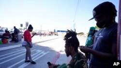 File - Jean Adler Cactus, right, a Haitian migrant seeking asylum in the United States, works on the hair of Haitian migrant Thomas Volcy, near an entrance to the border crossing, March 1, 2021, in Tijuana, Mexico