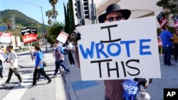 Justice Hardy, a writer on the television series "True Lies," holds up a sign as members of The Writers Guild of America picket outside Warner Bros. Studios, Tuesday, May 2, 2023, in Burbank, California.