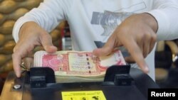 مردی در یک صرافی در بغداد، پایتخت عراق، اسکناس‌های دینارهای عراقی را روی دستگاه شمارش پول می شمرد.  ۲۳ ژانویه ۲۰۲۳