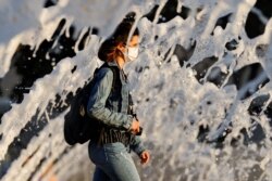 A woman wearing a face mask walks past a fountain amid the spread of the coronavirus disease, in San Diego, California, June 18, 2020.