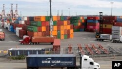 FILE - Trucks hauling shipping containers drive near containers stacked five-high at a terminal on Harbor Island in Seattle, Oct. 2, 2019.