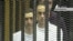 This video image taken from Egyptian State Television shows the sons of Hosni Mubarak, Alaa Mubarak, left and Gamal Mubarak as they stand inside the cage of mesh and iron bars in a Cairo courtroom Wednesday Aug. 3, 2011 as his historic trial began on c