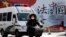 A woman and a police van pass a Chinese government propaganda billboard that reads "China Rule By Law" on a street in Beijing, Dec. 28, 2016. Many in China are infuriated by a decision to drop charges in a high-profile police brutality case.