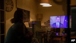 FILE - A woman watches the speech of King Felipe VI of Spain on television, in Bustarviejo, outskirts of Madrid, March 18, 2020.