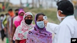 Seorang petugas memeriksa suhu tubuh pekerja migran sebelum diijinkan masuk ke kereta api yang akan membawa mereka kembali ke tempat asal mereka di Jammu, India, 11 JUni 2020. 