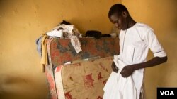 Abdulkadir Abdullahi arranges his school uniform in Maiduguri, Nigeria, October 2016. (C. Oduah/VOA)