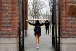 FILE - A student carries a box to her dorm at Harvard University, after the school asked its students not to return to campus after Spring Break and said it would move to virtual instruction, in Cambridge, Massachusetts, March 10, 2020.