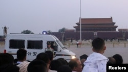 Seorang polisi paramiliter berjaga di depan sebuah mobil polisi saat para pengunjung menunggu upacara penaikan bendera di Alun-alun Tiananmen saat matahari terbit di Beijing, China, 4 Juni 2019.
