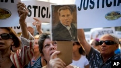 FILE - A woman sings the Argentine national anthem while holding a portrait of the late prosecutor Alberto Nisman outside the AMIA Jewish community center in Buenos Aires, Jan. 21, 2015.