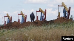 Seorang pekerja berdiri di depan pompa angguk minyak di lapangan minyak Ashalchinskoye yang dimiliki perusahaan Rusia, Tatneft, dekat Almetyevsk, Republik Tatarstan, Rusia, 27 Juli 2017.