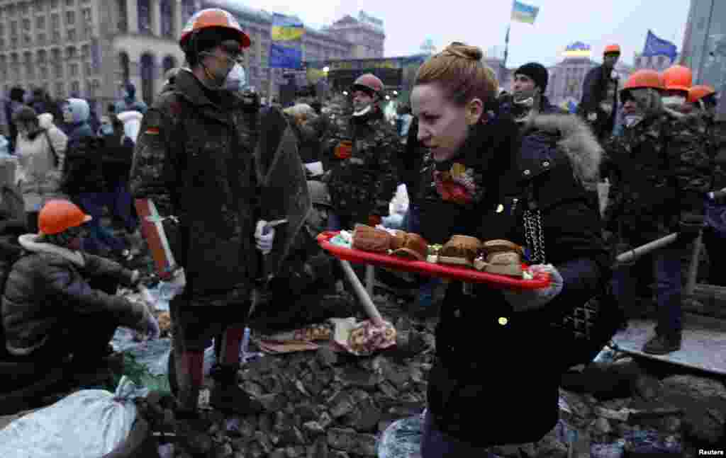 Seorang perempuan membawa roti lapis di tengah demonstrasi anti-pemerintah di alun-alun ibukota Kyiv (19/2). (Reuters/David Mdzinarishvili)
