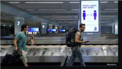 Travelers at LaGuardia Airport, New York, pass a sign alerting them to social distance during the outbreak of the coronavirus, June 29, 2020.